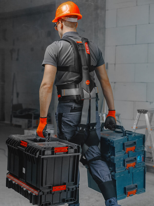 Exoskelett Hunic SoftExo Lift – Arbeiter trägt Werkzeugkisten auf Baustelle